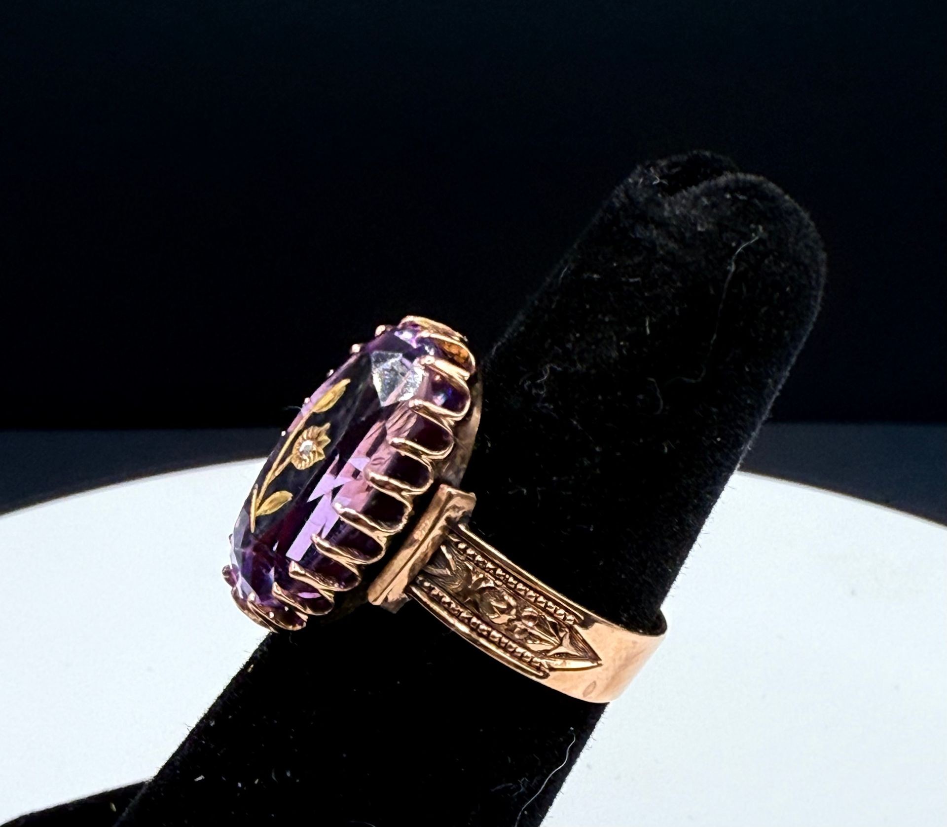 The ring is crafted from 14k rose gold and features a large, oval-cut amethyst as its centerpiece. A small diamond is set within a floral design that is carved into the amethyst. The band of the ring has a filigree design, adding to its vintage aesthetic.  Details: Metal: 14k Rose Gold Gemstone: Oval-cut Amethyst Accent Stone: Small Diamond Design: Carved floral design within the amethyst, filigree detailing on the band Style: Vintage, possibly Art Deco inspired  Amethyst is a type of quartz and is known as the stone of spirituality and intuition. It is believed to promote balance and connection to one's inner self. 